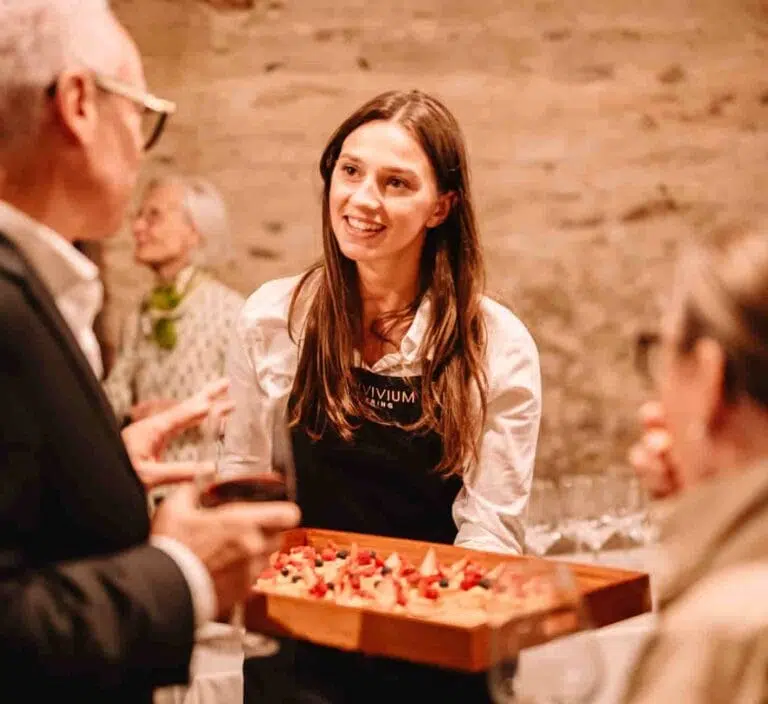 Cameriera con grembiule Convivium Catering durante un aperitivo con in mano un vassoio di antipasti